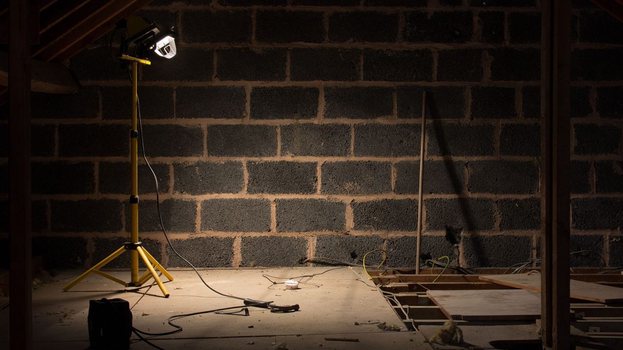Unfinished attic lit by a work light with cable runs across the floor