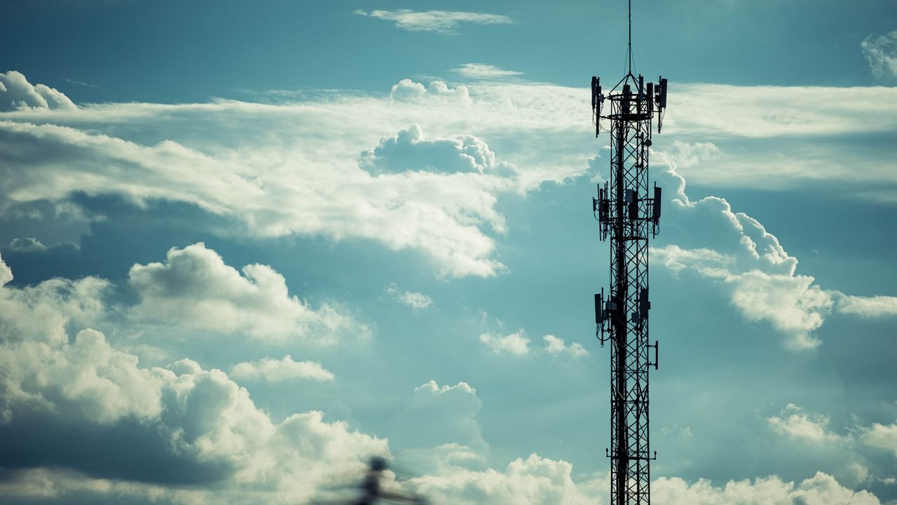 Cellular tower with panel antennas silhouetted against blue sky and clouds