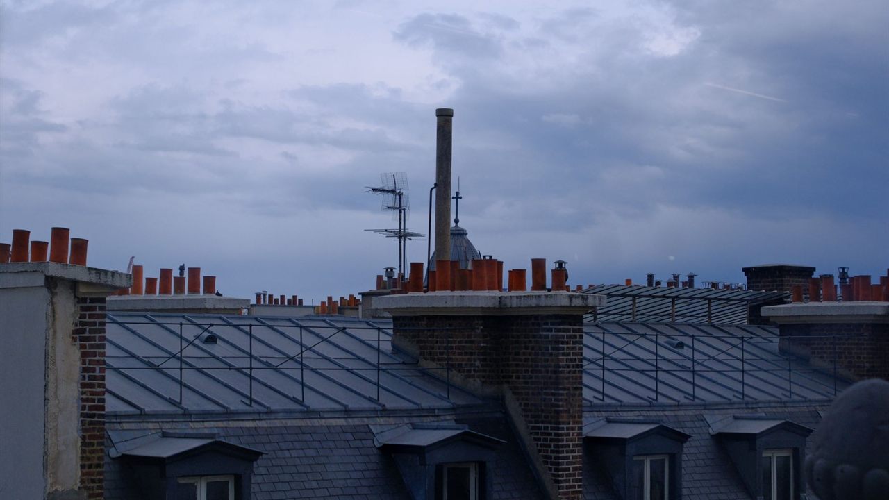 Antenna mast beside a brick chimney stack on a city roof