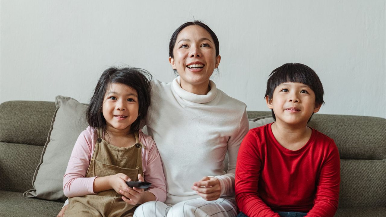 Mother and two children on a sofa watching television with a remote