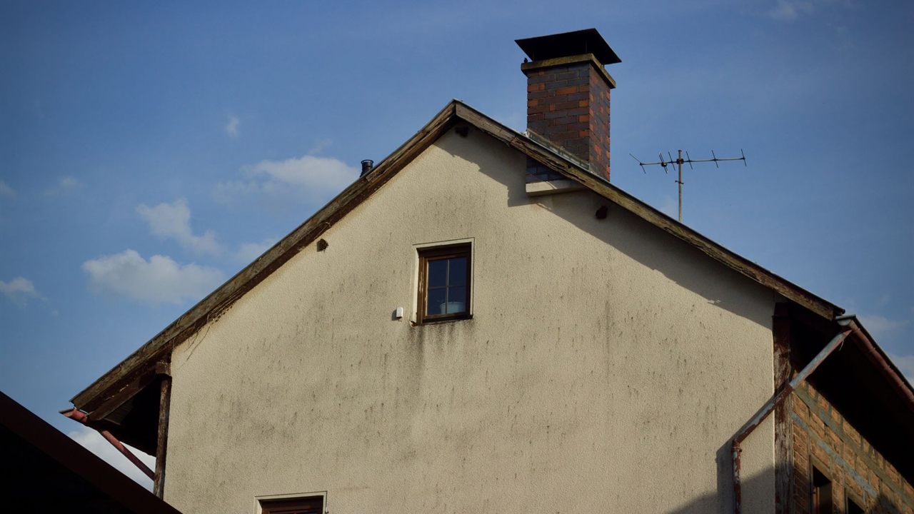 Gable end of a stucco house with a brick chimney and a Yagi TV antenna on the roof