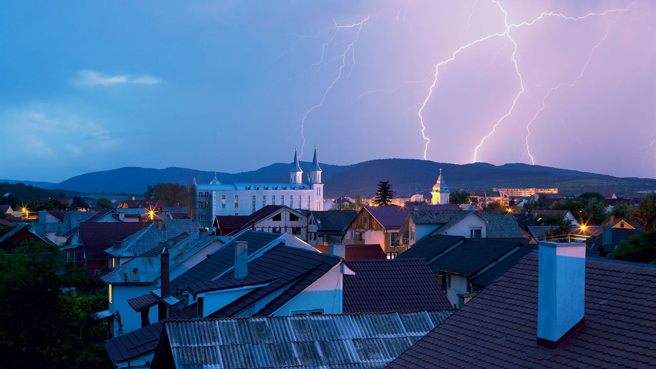 Lightning strikes behind a town of pitched roofs at dusk