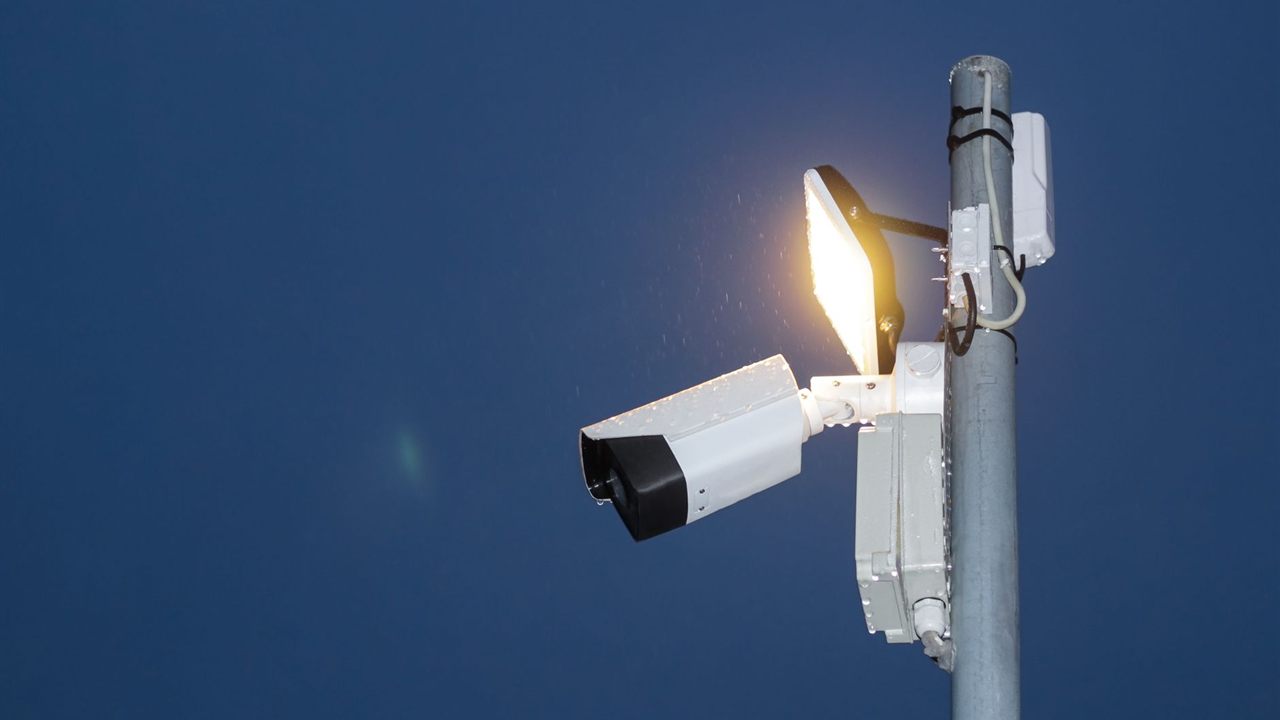 Bullet security camera on a pole at night beside a floodlight, when night power draw peaks