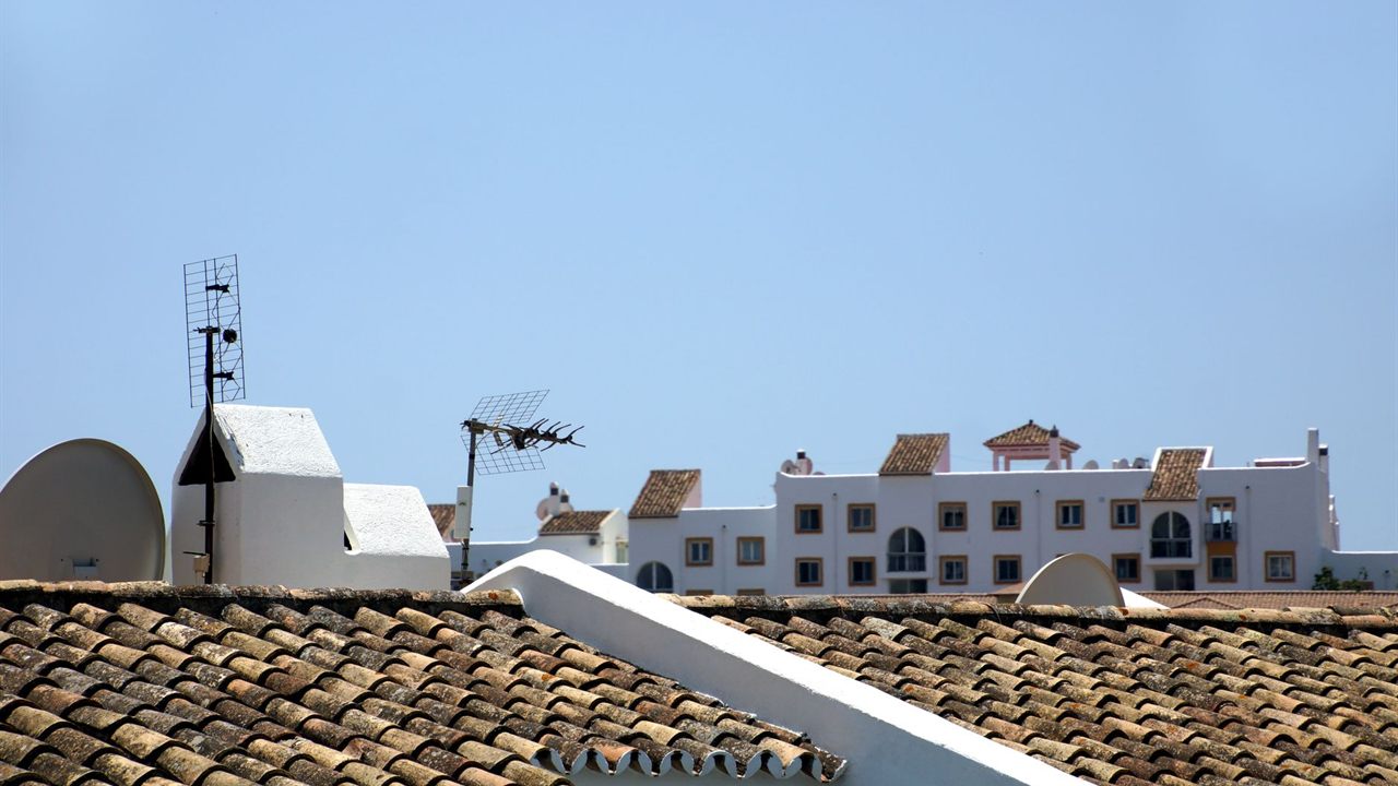 Tiled rooftops with TV antennas on short masts against a clear sky