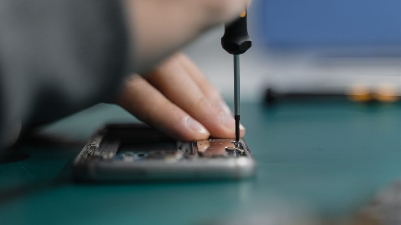 Technician driving a small screw on an opened electronic device
