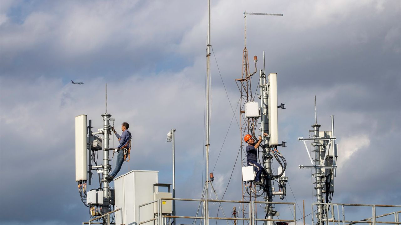 Two technicians in harnesses working on rooftop antenna masts